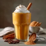 Pumpkin spice protein shake served with whipped coconut cream and cinnamon stick on a wooden table.
